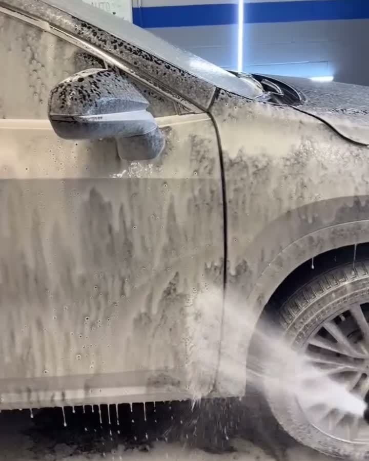 SUV covered in thick white foam during a foam hand wash, water running off the rocker panel